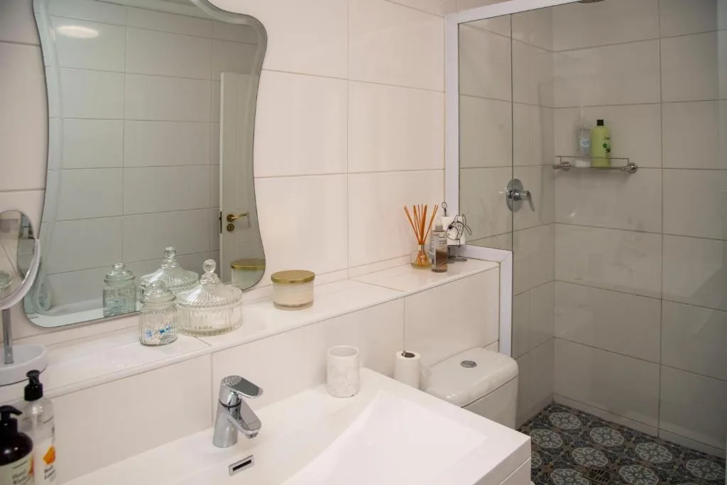 Clean modern bathroom with white tiles, vanity mirror, and glass shower enclosure
