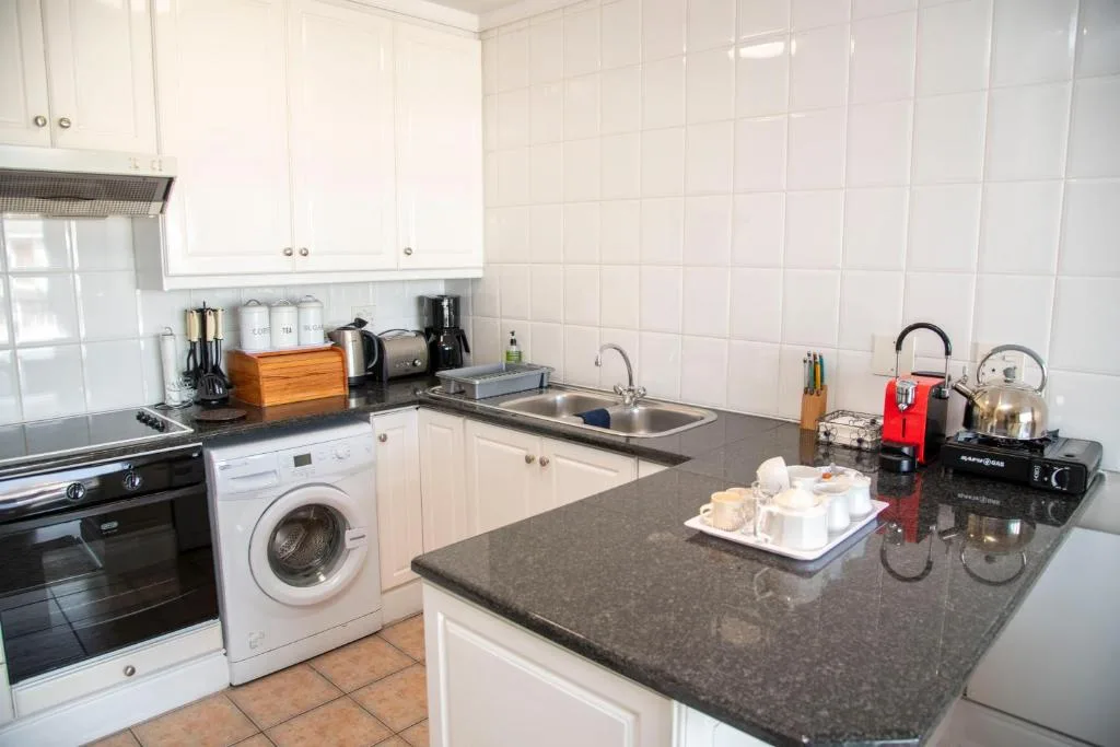White kitchen with dark countertop, stove, washing machine, and sink