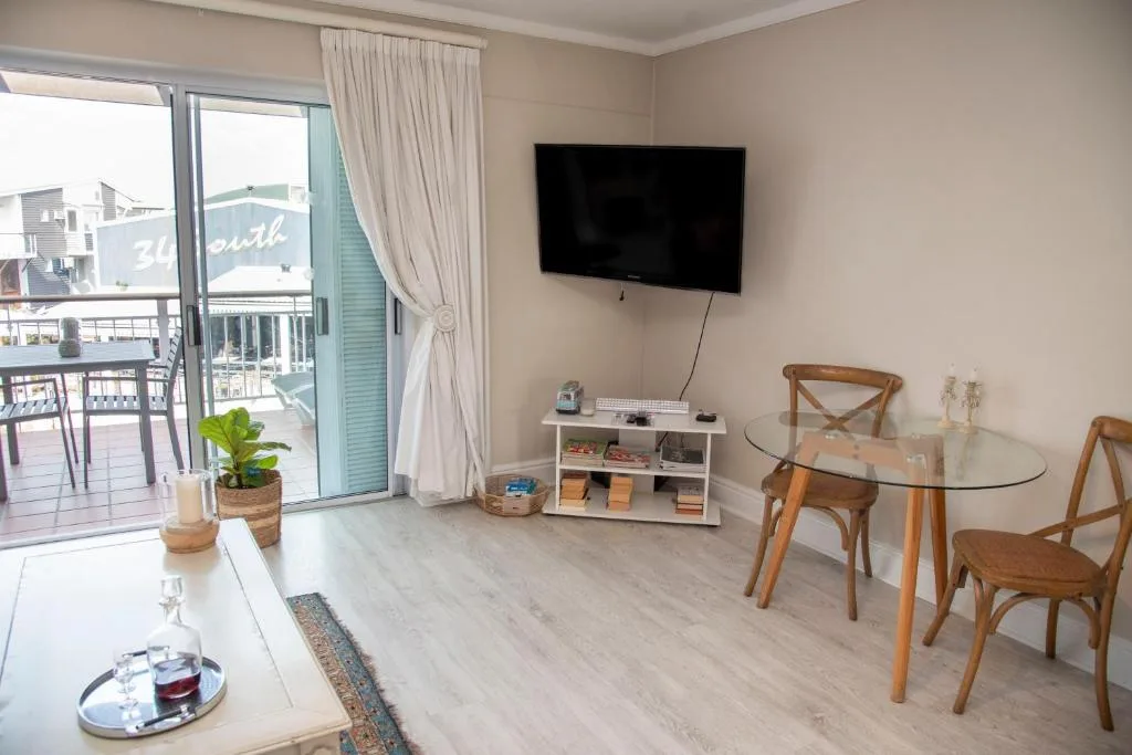 Modern living room with wall-mounted TV, glass dining table, and waterfront views