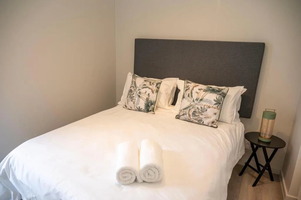 Neatly made bed with rolled towels and decorative pillows on dark headboard