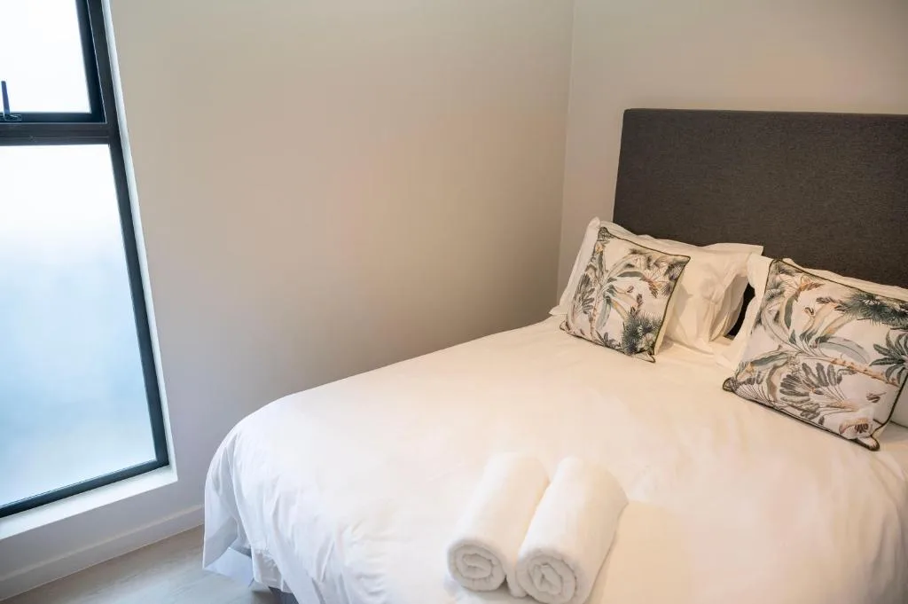 Spacious bedroom with queen bed, dark headboard, patterned pillows, rolled towels