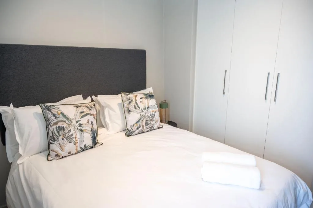 Modern bedroom with dark headboard, white bedding, and patterned cushions