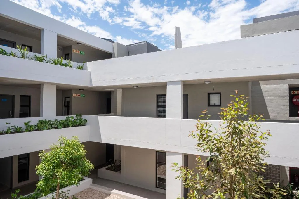 Modern white apartment building with tiered balconies and landscaped courtyard