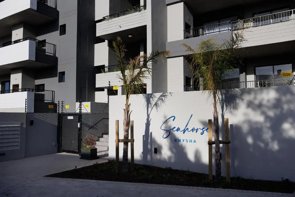Modern white apartment building entrance with Seahorse Knysna signage and palm trees