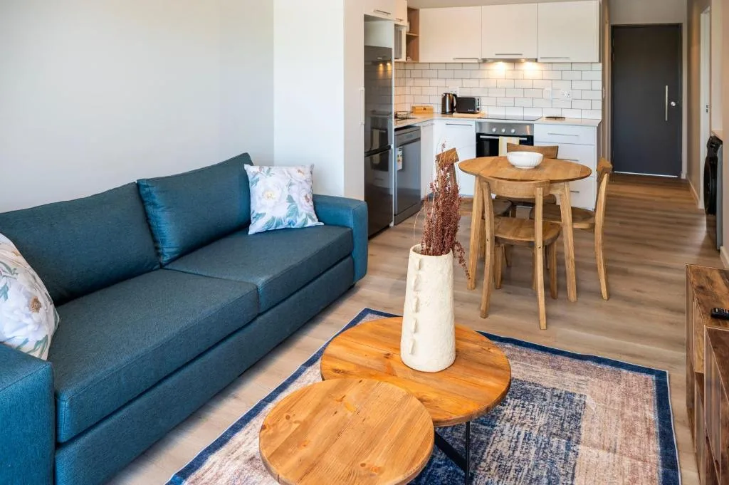 Modern lounge with teal sofa, wooden coffee table, and open-plan kitchen