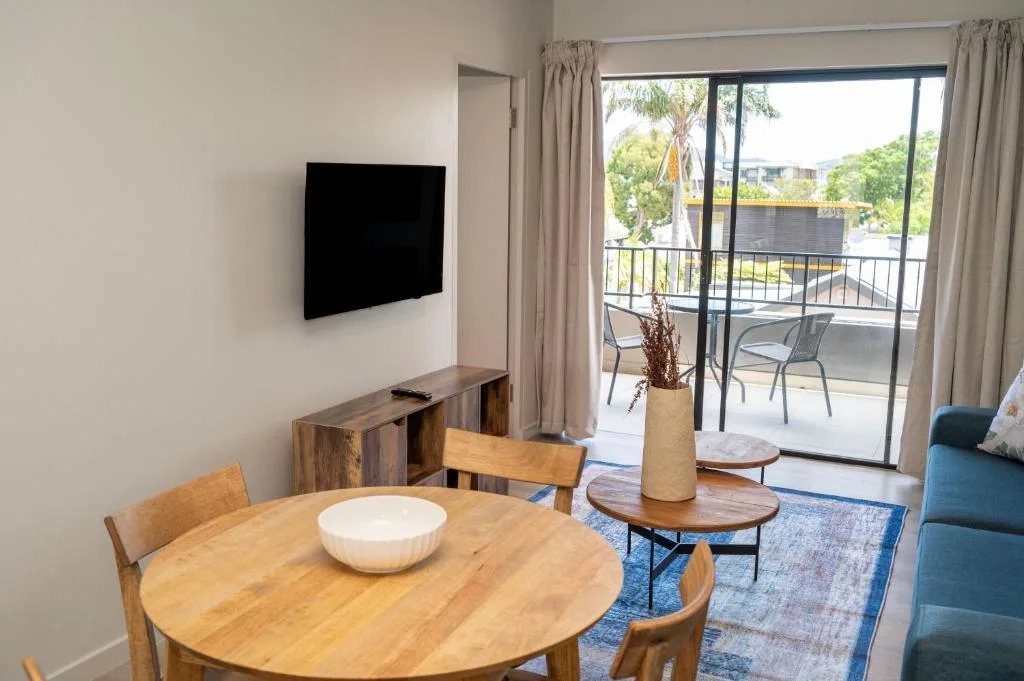 Open-plan lounge with TV, dining table, and deck access overlooking garden