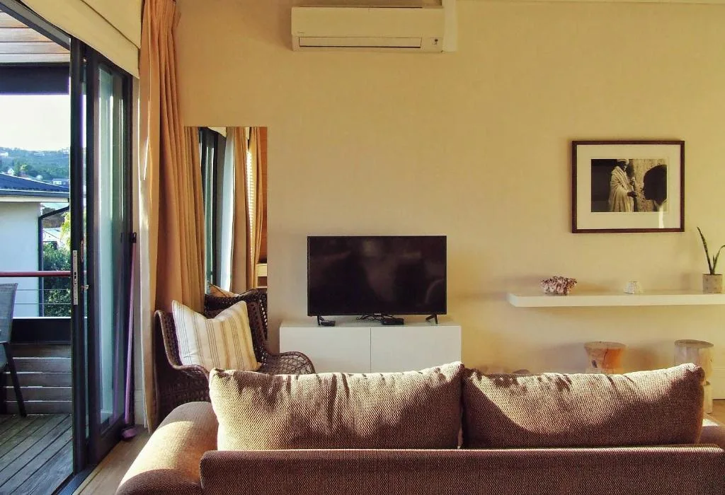 Bright living room with brown sofa, flat-screen TV, and scenic deck access