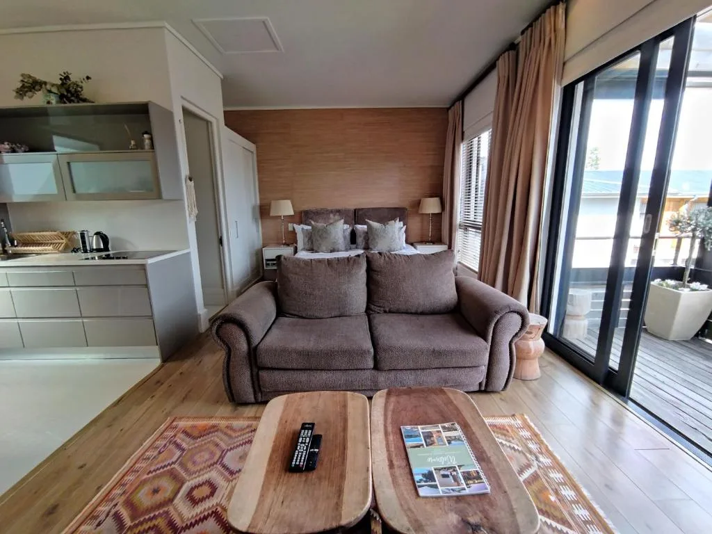 Modern studio lounge with sofa, wooden coffee table, and ocean views through glass doors