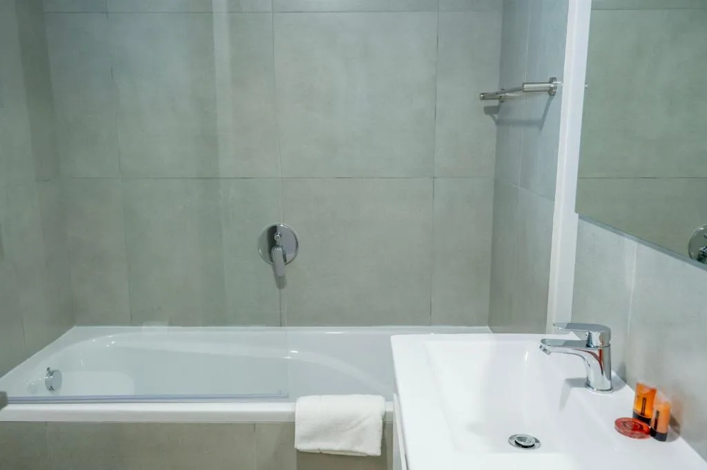 Modern bathroom with white bathtub, basin, and pale green tiled walls