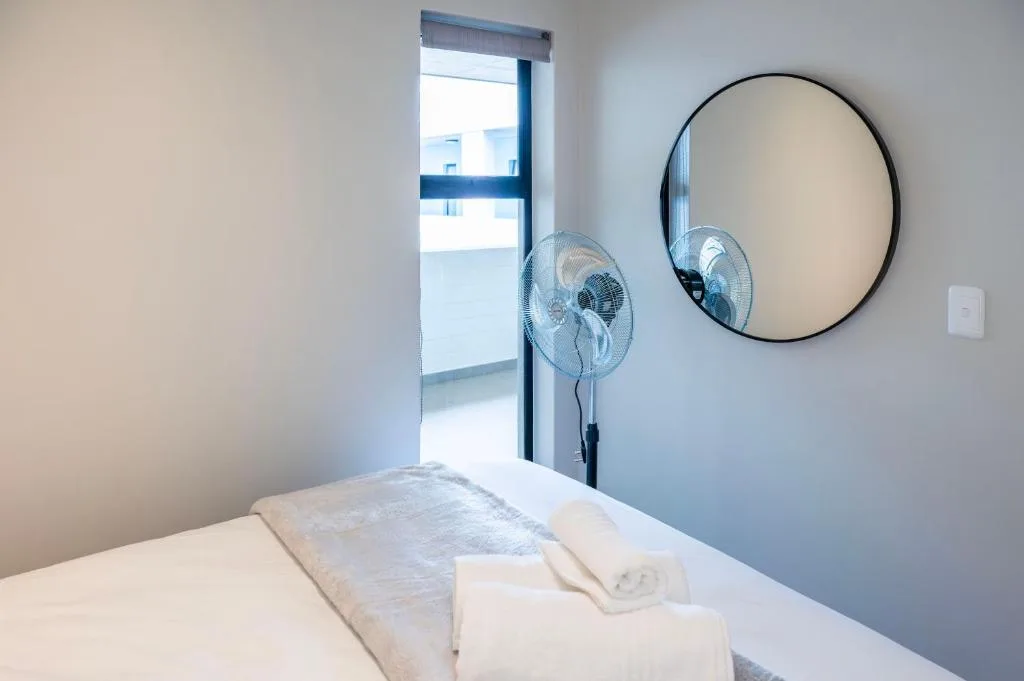 Bright bedroom with bed, round mirror, and standing fan by door