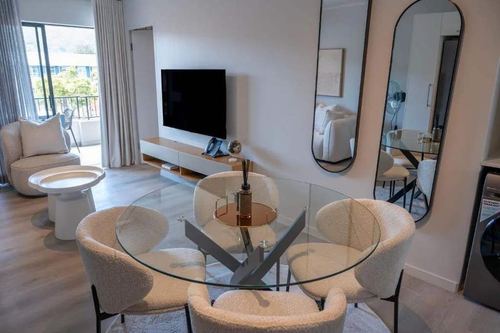 Modern living room with curved cream chairs, glass dining table, and wall-mounted TV