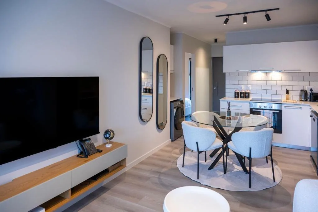 Open-plan lounge with TV, dining table, and modern kitchen visible