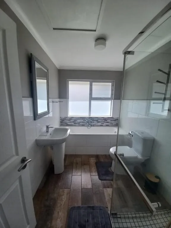 Modern bathroom with pedestal sink, bathtub, and glass shower enclosure