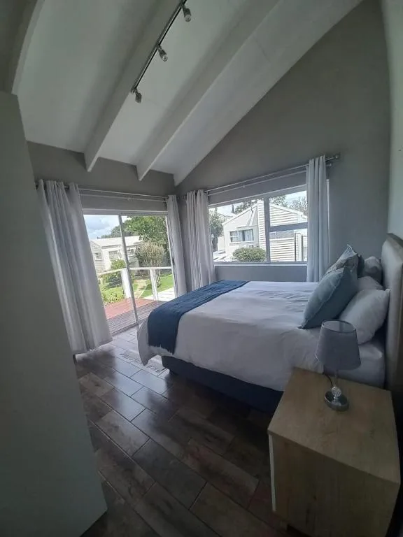 Bright bedroom with queen bed, large windows overlooking garden, modern ceiling beams