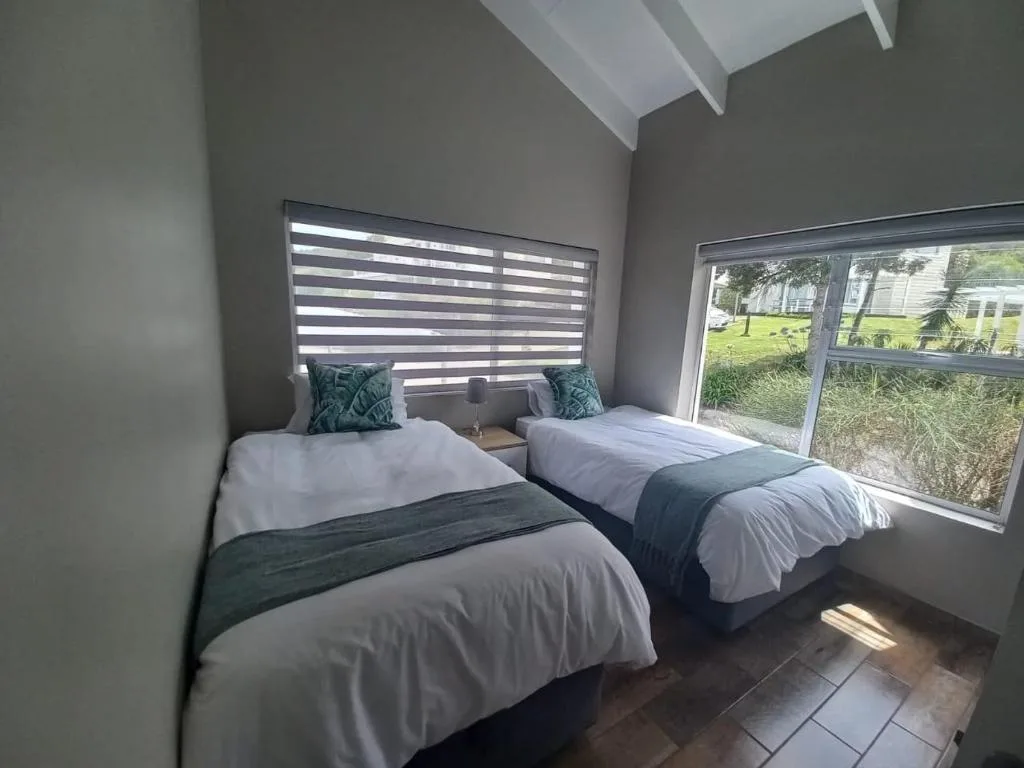Twin bedroom with white bedding, striped blinds, and garden views