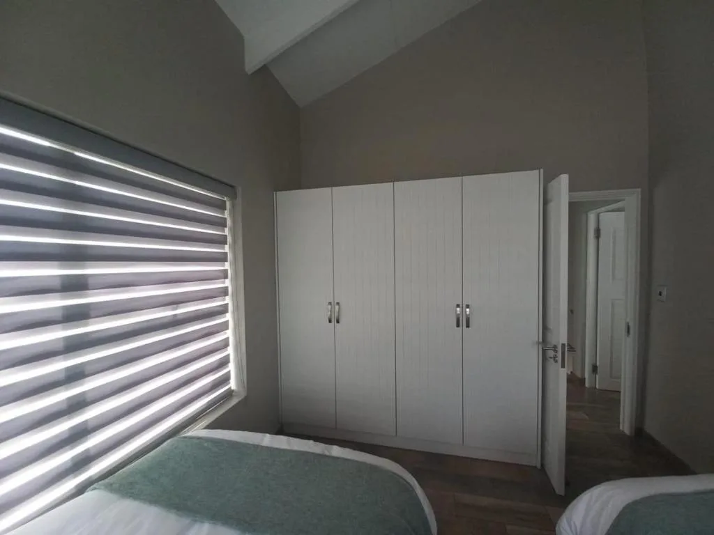Modern bedroom with dual beds, white built-in wardrobes, and striped window blinds