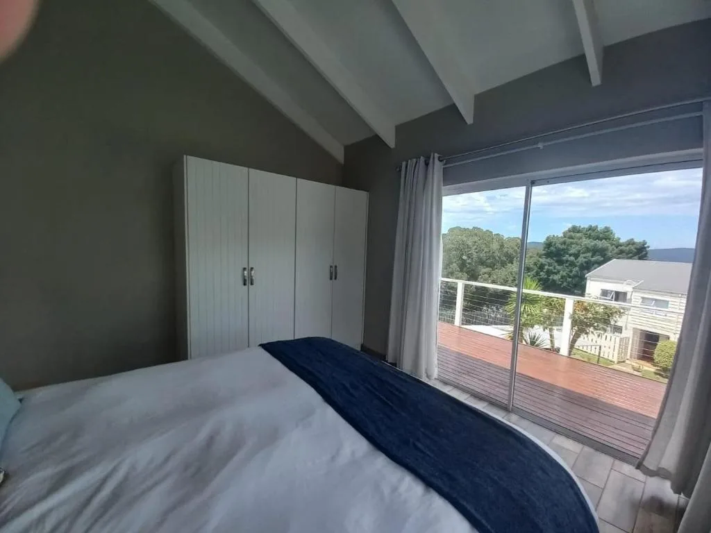 Modern bedroom with queen bed, built-in wardrobes, and scenic lagoon views through glass doors