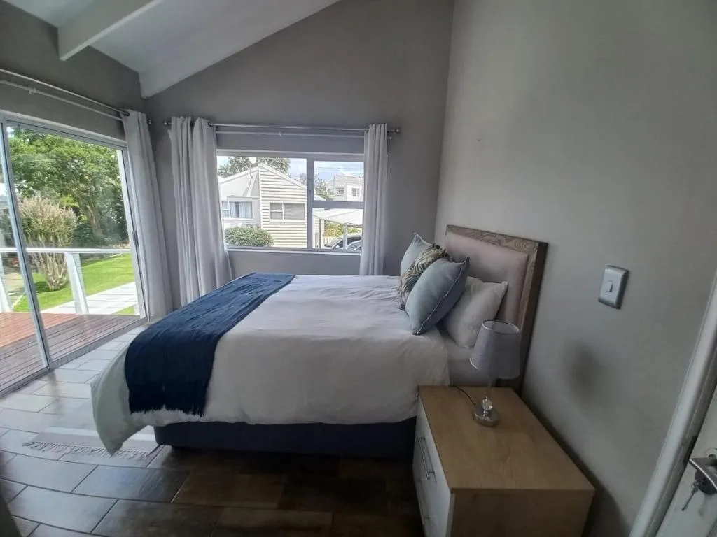 Bright bedroom with queen bed, large windows overlooking garden and deck area
