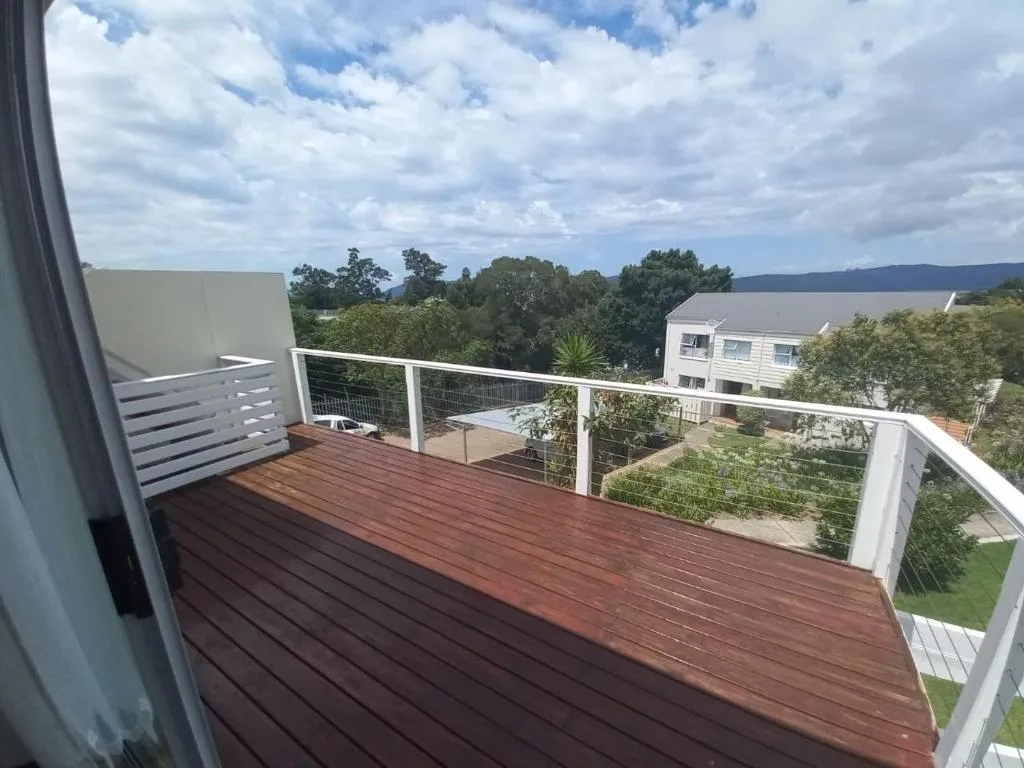 Spacious wooden deck with white railing overlooking garden route landscape