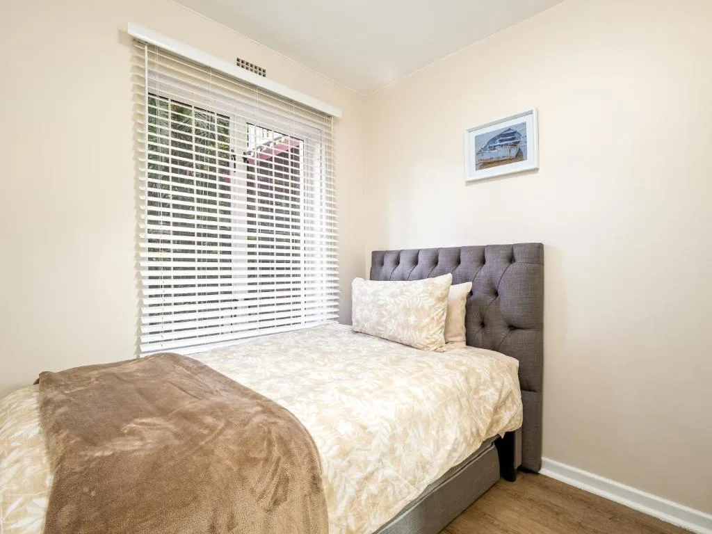 Bright bedroom with queen bed, gray upholstered headboard, and plantation shutters