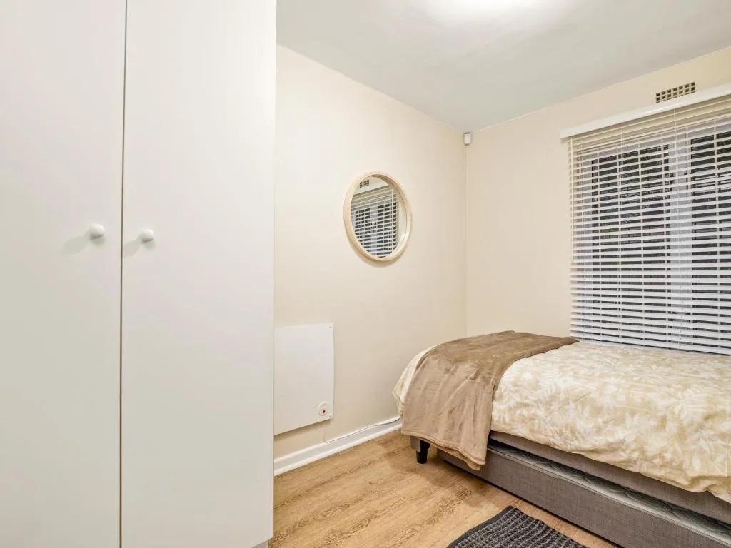 Bright bedroom with double bed, white wardrobe, and wooden flooring