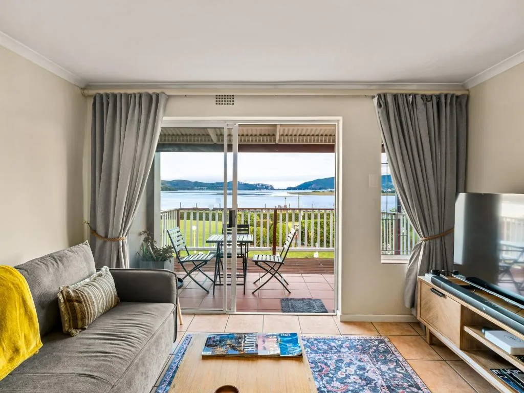 Spacious lounge with gray sofa overlooking lagoon and mountains through glass doors
