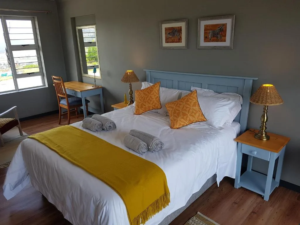 Bright bedroom with queen bed, blue headboard, orange cushions, rolled towels