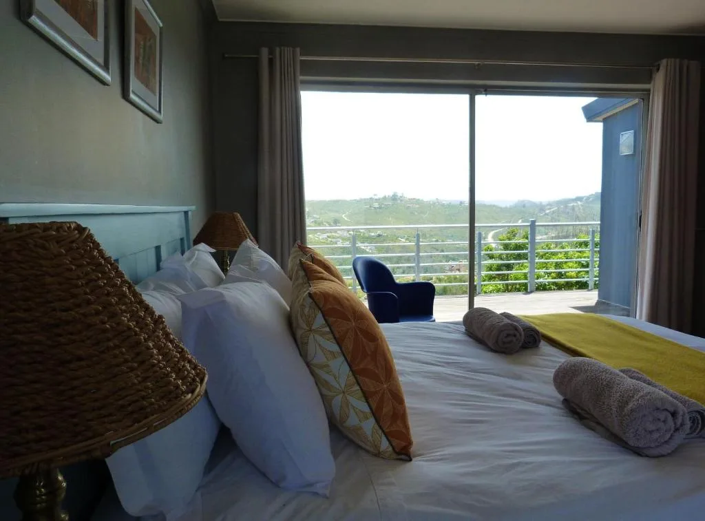 Bedroom with bed, pillows, rolled towels, and scenic hillside views through glass doors