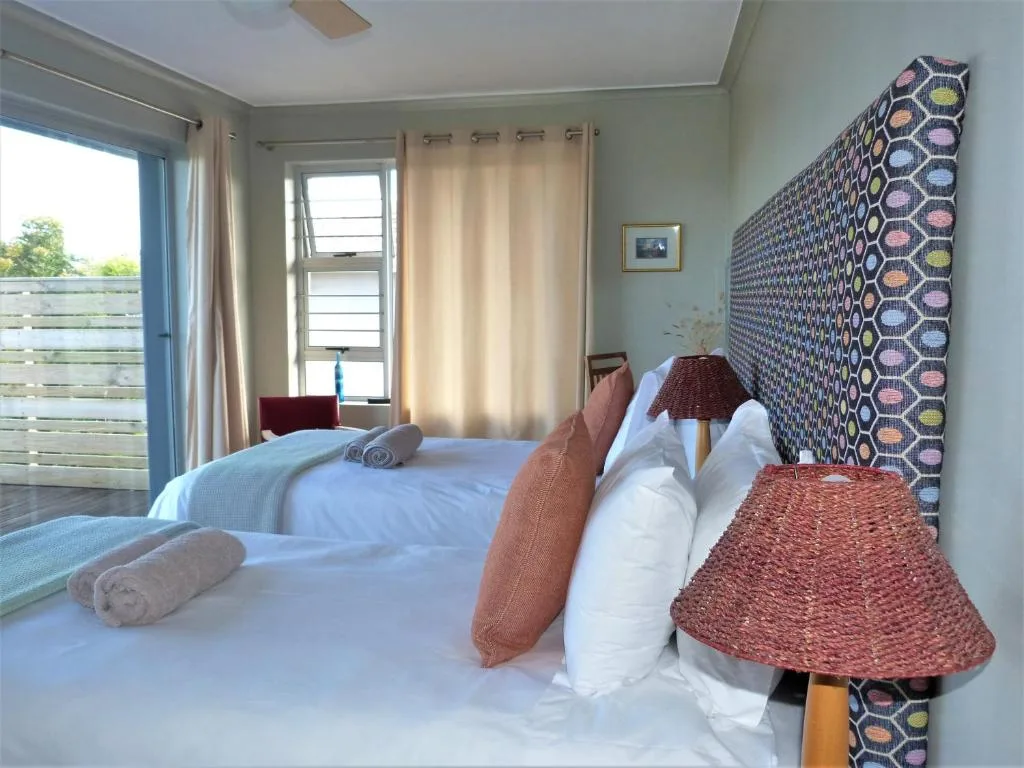 Bright bedroom with twin beds, patterned headboard, and deck access