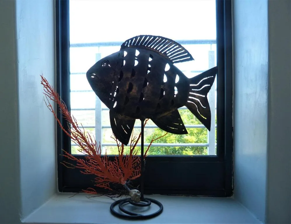 Black fish sculpture with red coral detail on windowsill, lagoon view beyond