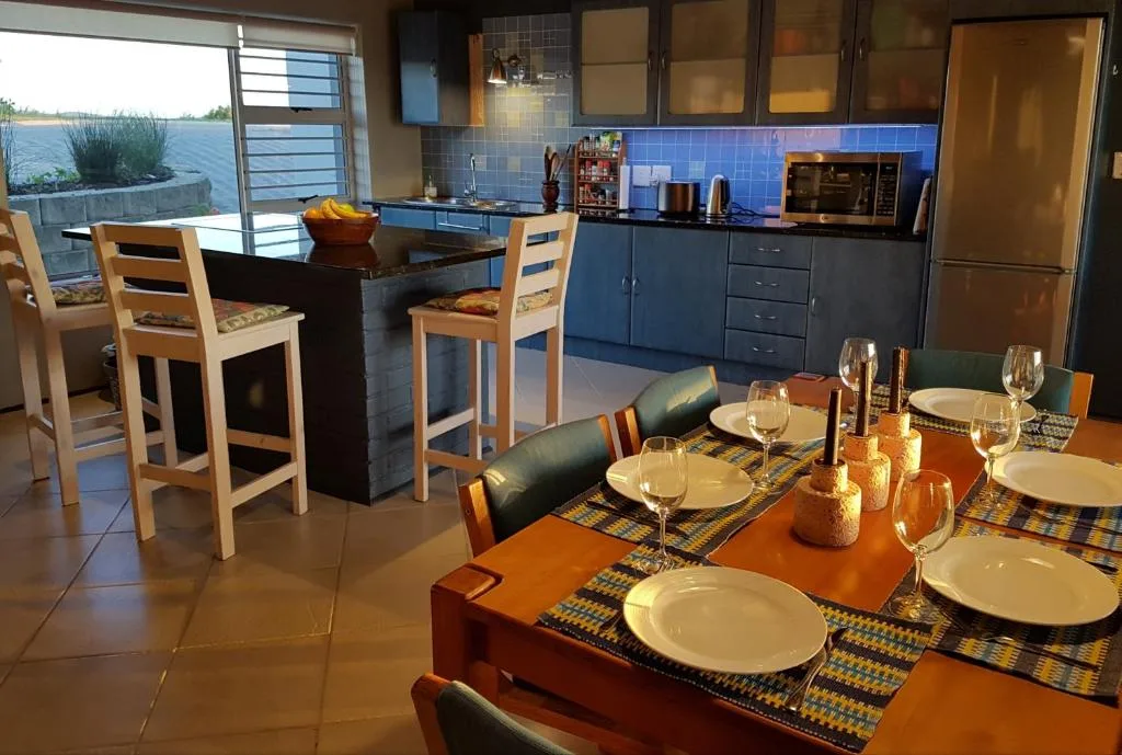 Dining table set for meal with water view and open kitchen beyond