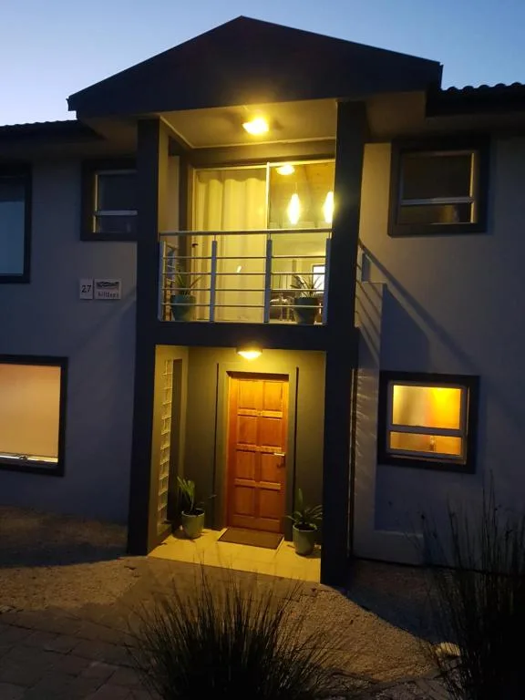 Modern two-story house exterior with wooden door and lit balcony at dusk