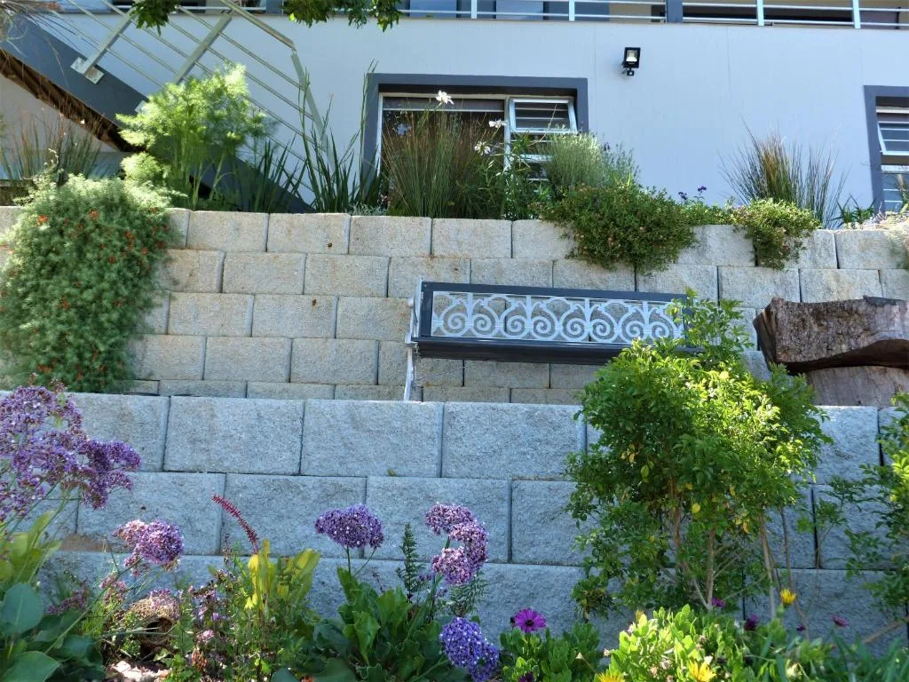 Modern white building with tiered stone retaining wall and flowering garden beds