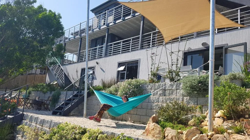 Modern multi-level holiday home with yellow shade sail and turquoise hammock in garden