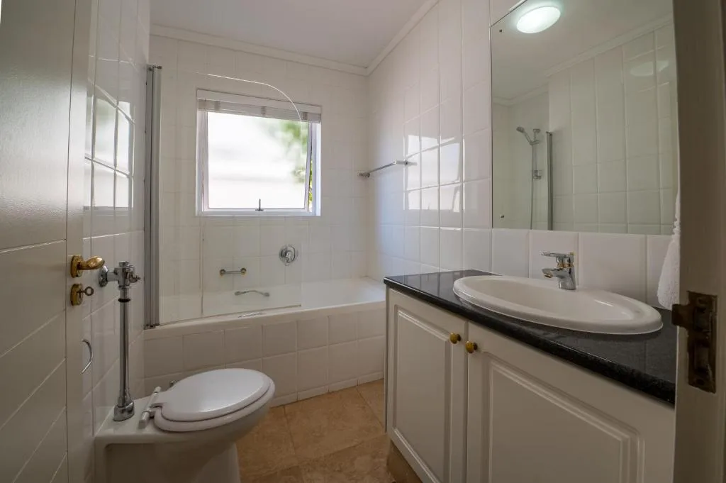 Spacious bathroom with toilet, vanity sink, and glass-enclosed shower tub