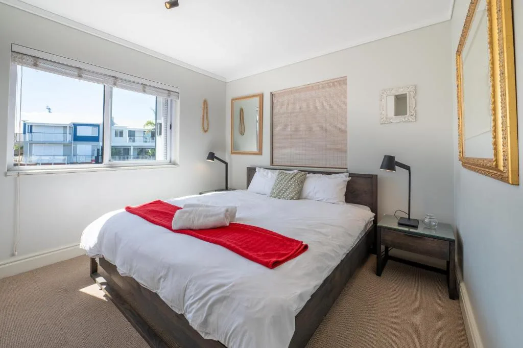 Bright bedroom with queen bed, red throw, and large window overlooking Knysna marina