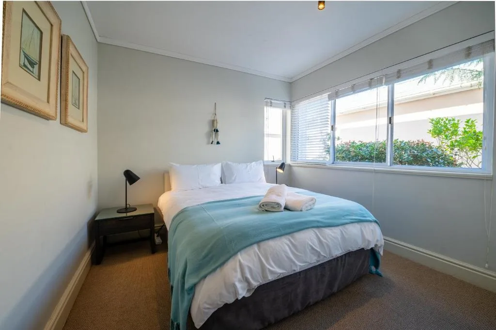 Bright bedroom with made bed, side table lamp, and garden views through windows
