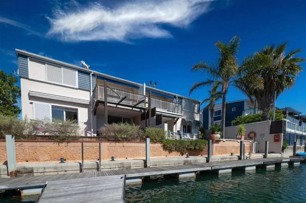 Waterfront house with wooden deck and palm trees, clear blue sky