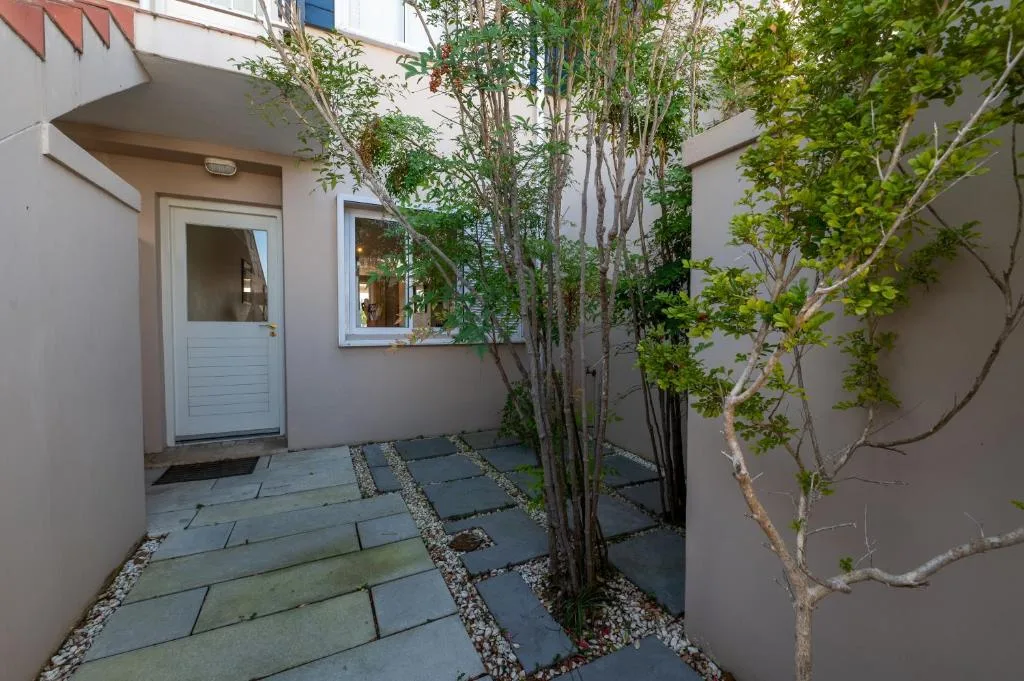 Modern courtyard entrance with stone paving, white door, and climbing vines