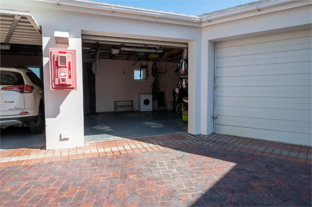 Modern white-walled garage and driveway with brick paving and red emergency box