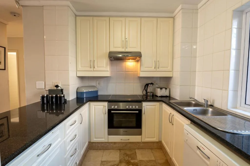 Well-equipped kitchen with cream cabinets, black countertops, and stainless steel appliances