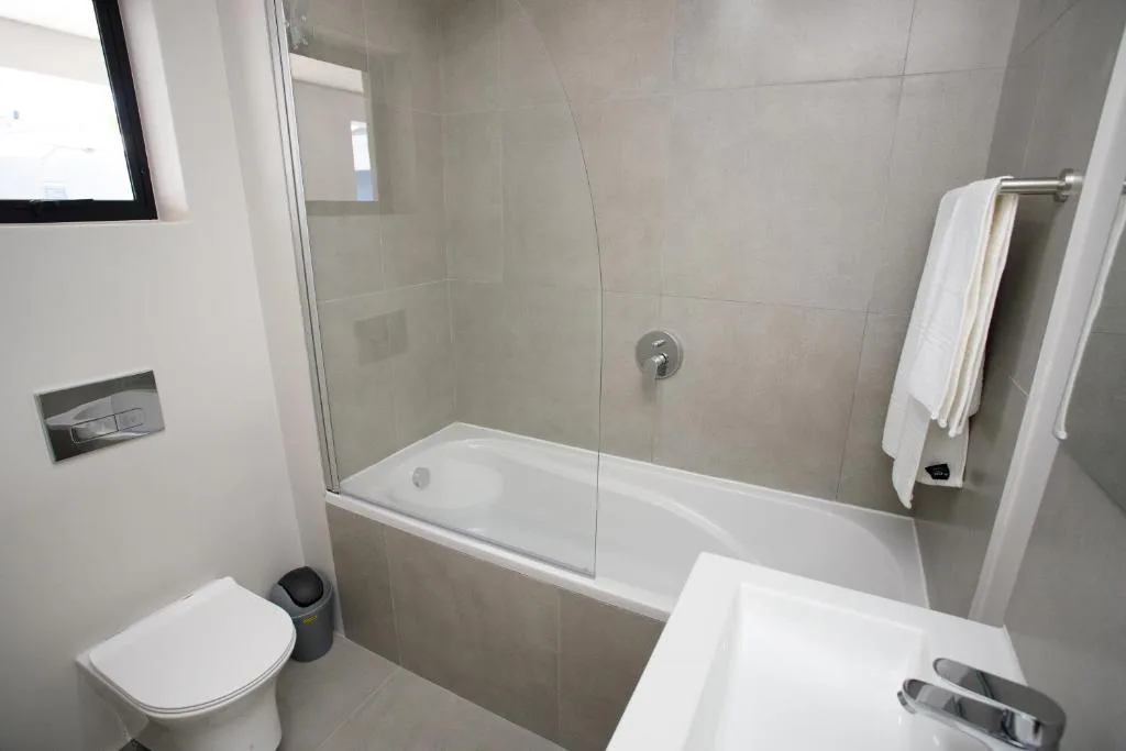 Modern bathroom with glass shower enclosure, white bathtub, toilet, and towel rail