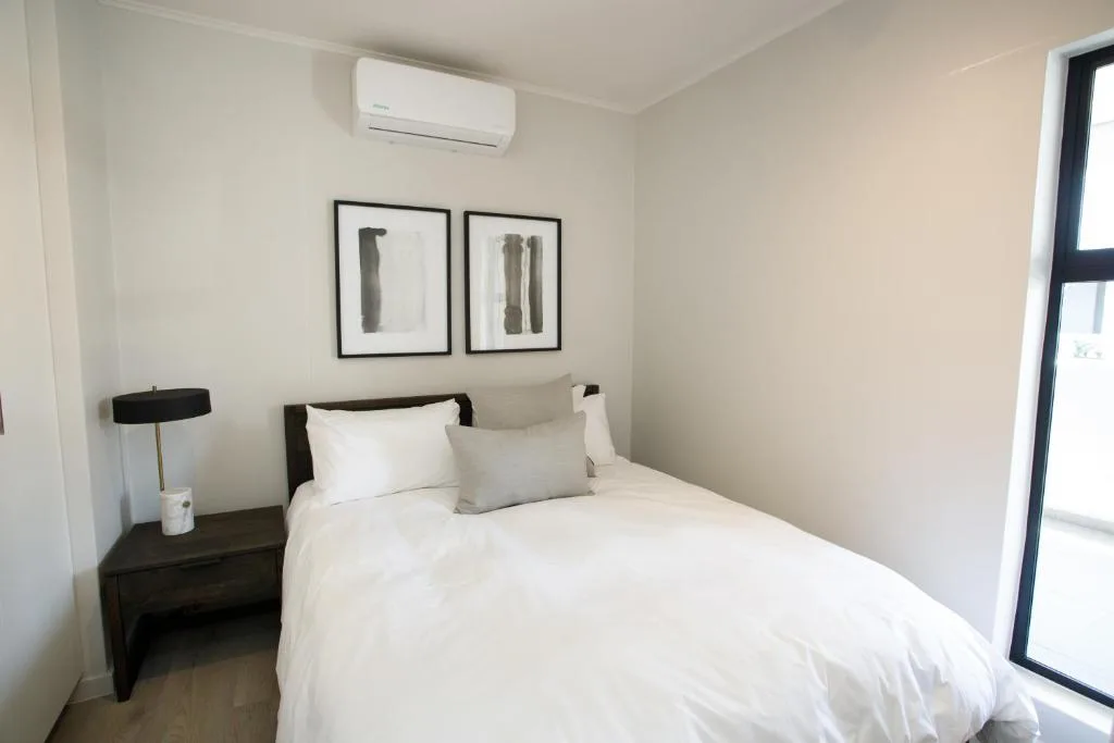 Modern bedroom with white bedding, black nightstand, and minimalist wall art