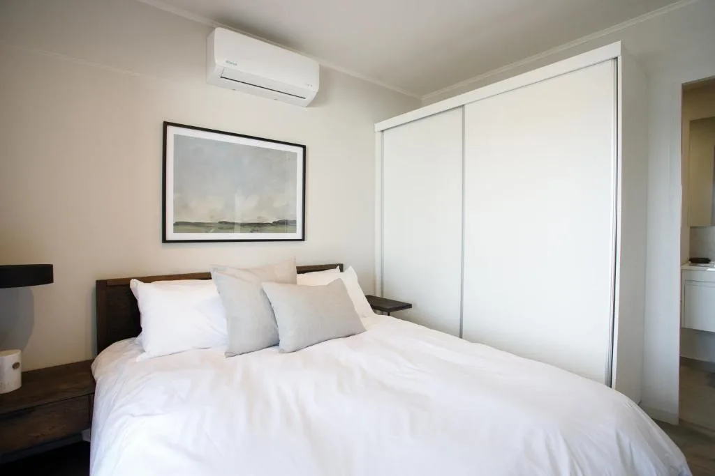 Bright bedroom with white bedding, dark wood headboard, framed landscape artwork
