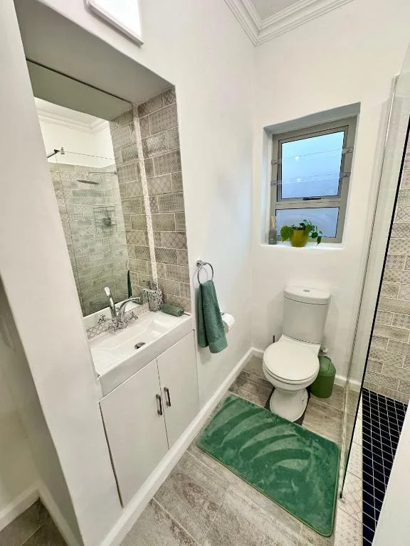 Modern bathroom with shower, vanity, toilet, and window with green accents