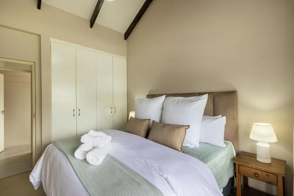 Bright bedroom with queen bed, white pillows, wooden nightstand with lamp