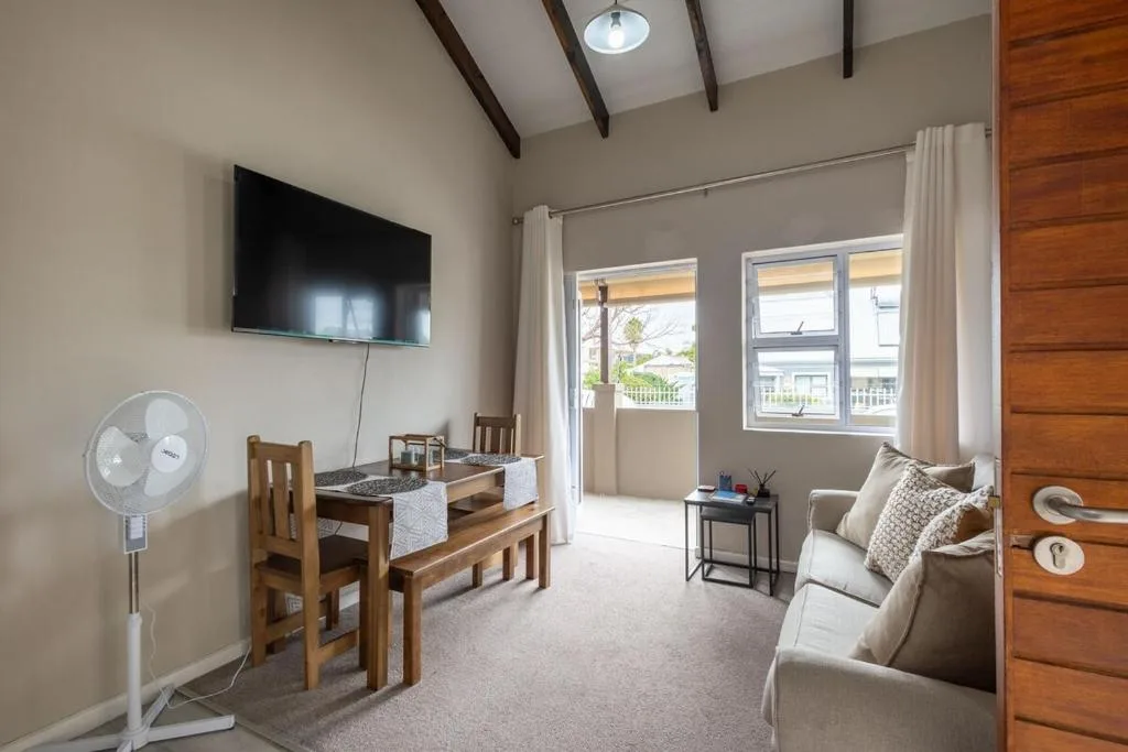 Modern lounge with TV, sofa, dining table, and balcony doors overlooking garden