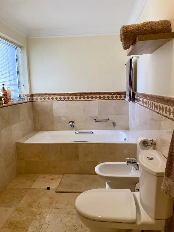 Spacious bathroom with bathtub, toilet, bidet, and beige tile finishes