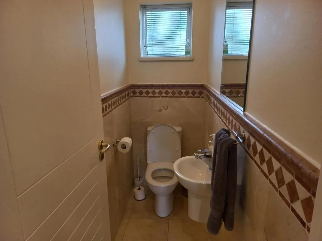 Compact bathroom with toilet, pedestal sink, and decorative tile border