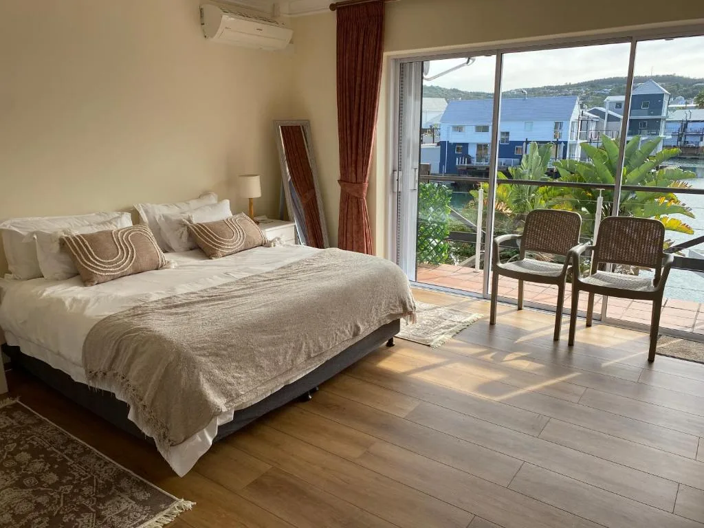 Spacious bedroom with waterfront view through glass doors, featuring a bed and seating area